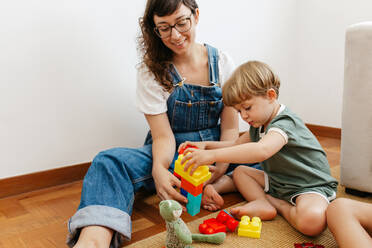 Cute child playing with colorful blocks with his mother sitting by. Kid playing with colorful toys with mother at home. - JLPSF03599