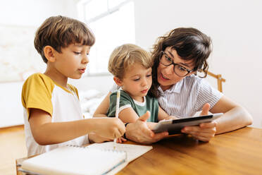 Frau zeigt ihren Kindern zu Hause etwas Interessantes auf einem digitalen Tablet. Jungen benutzen mit ihrer Mutter ein digitales Tablet. - JLPSF03606