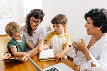 Glückliche LGBT-Familie zu Hause: Ein lesbisches Paar sitzt mit seinen Kindern vor einem digitalen Tablet. - JLPSF03608