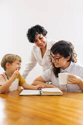 Cute boy looking at his mother and smiling while sitting at table. Female couple spending time with their son at home. - JLPSF03619