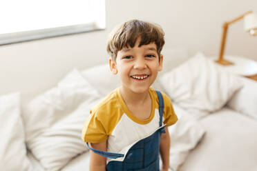 Porträt eines glücklichen kleinen Jungen, der auf der Couch sitzt und in die Kamera schaut und lächelt. - JLPSF03650