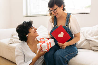 Eine Frau gibt ihrer Partnerin ein Geschenk und eine Karte zum Valentinstag. Ein lesbisches Paar feiert einen besonderen Tag mit einem Geschenk und einer Grußkarte. - JLPSF03669