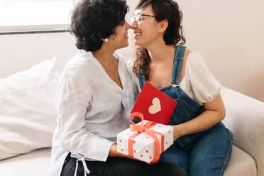 Zwei Frauen halten ein Valentinsgeschenk und eine Valentinskarte in der Hand und wollen sich küssen. - JLPSF03671