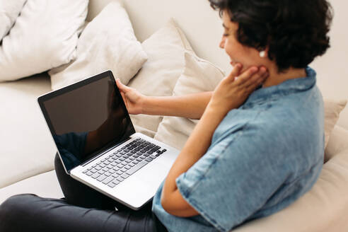 Woman sitting on sofa with a laptop. Female holding laptop with blank screen and smiling. - JLPSF03674