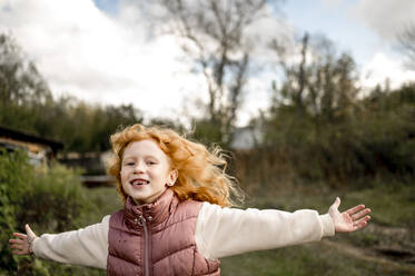 Happy girl running with arms outstretched in garden - ANAF00151