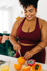 Beautiful female making healthy juice in kitchen. Fitness woman cutting fruits for preparing juice at home. - JLPSF03724