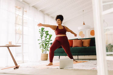 Full length of plus size woman stretching at home. Female in sports clothing doing yoga in living room. - JLPSF03755