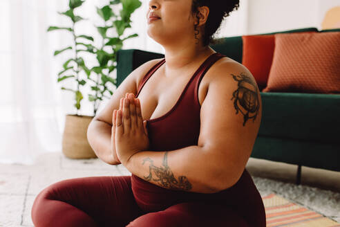 Abgeschnittene Aufnahme einer gesunden Frau, die im Wohnzimmer Yoga macht. Frau in Sportkleidung macht Workout, während sie auf dem Boden sitzt. - JLPSF03769