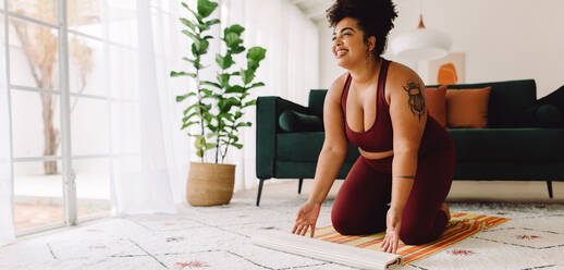Weitwinkelaufnahme von plus size Frau setzen Yogamatte auf dem Boden zu Hause für das Training. Gesunde weibliche Beginn Yoga-Training zu Hause. - JLPSF03772