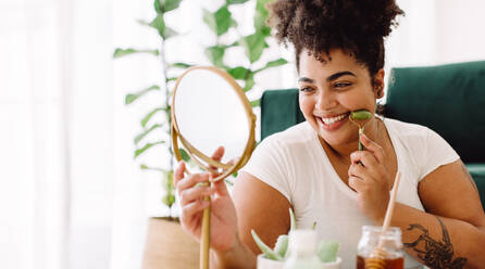 Pretty woman taking care of facial skin by using massage tools while  looking at mirror. Female