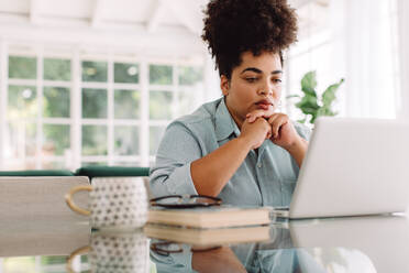 Attractive female sitting on table and looking at laptop. Businesswoman working from home. - JLPSF03834