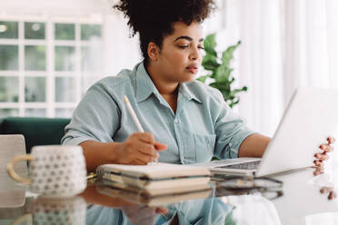 Woman working on laptop and taking notes in a book. Business woman working from home. - JLPSF03838