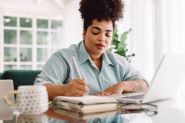 Female writing notes while sitting at desk with laptop. Businesswoman sitting at desk working from home office. - JLPSF03840