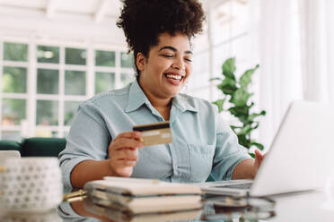Frau lächelnd, während tun Online-Zahlung zu Hause. Frau hält Kreditkarte und mit Laptop für Online-Shopping. - JLPSF03846