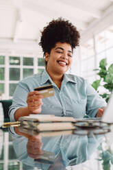 Frau lächelnd beim Bezahlen für Online-Shopping mit Kreditkarte. Fröhliche Frau sitzt am Schreibtisch mit Kreditkarte. - JLPSF03848