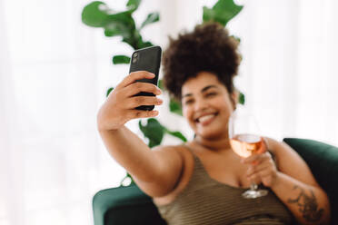 Frau nimmt Selfie auf Smartphone zu Hause mit einem Weinglas. Frau hält ein Glas Wein und nimmt Selfie. - JLPSF03859
