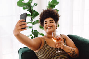 Attraktive Frau, die ein Selfie mit dem Handy macht, während sie ein Glas Wein in der Hand hält. Eine Frau lächelt und hält ein Smartphone, um ein Selfie zu machen. - JLPSF03860