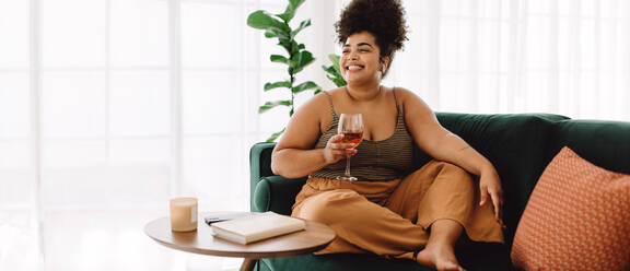 Attractive woman smiling with glass of wine. Female smiling and holding wine glass sitting on couch at home. - JLPSF03865