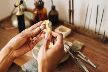 Nahaufnahme der Hände einer Juwelierin, die mit einem Messschieber in einer Schmuckwerkstatt die Größe eines Schmuckstücks misst. - JLPSF03908