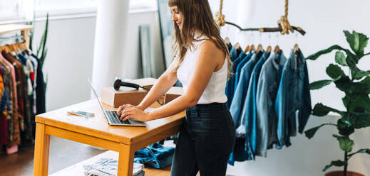 Junge Unternehmerin, die einen Laptop benutzt, während sie in ihrem Bekleidungsgeschäft arbeitet. Inhaberin eines Online-Shops, die Bestellungen auf ihrer Website entgegennimmt. Junge Unternehmerin, die ein kleines E-Commerce-Geschäft betreibt. - JLPSF03935