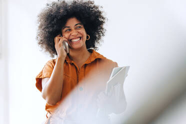 Ethnische Geschäftsfrau, die fröhlich lächelt, während sie ein Telefongespräch führt. Fröhliche Unternehmerin, die mit ihren Geschäftspartnern kommuniziert, während sie in einem modernen Büro arbeitet. - JLPSF03951