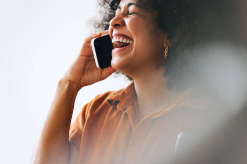 Geschäftsfrau, die fröhlich lacht, während sie ein Telefongespräch führt. Fröhliche Unternehmerin, die mit ihren Geschäftspartnern kommuniziert, während sie in einem modernen Büro arbeitet. - JLPSF03952