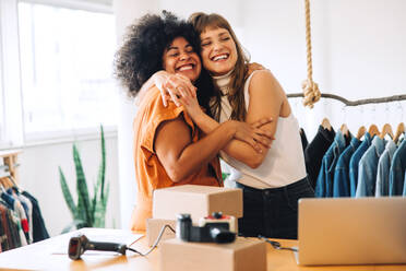 Glückliche Secondhand-Ladenbesitzerinnen, die sich fröhlich umarmen. Zwei junge Geschäftsfrauen, die ihren Erfolg als Team feiern. Zwei Unternehmerinnen, die ein kleines E-Commerce-Unternehmen führen. - JLPSF03981