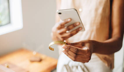 Cropped shot of female hands in studio taking photo of handmade ornament piece. Hands of jewelry seller in home shop using phone for online selling ornaments. - JLPSF04158