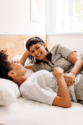 Couple chatting cheerfully while lying in bed. Happy young lesbian couple smiling while having a chat together in their bedroom. Young LGBQ+ spending quality time together at home. - JLPSF04174