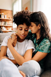 Queer couple bonding fondly. Two affectionate young lesbian women embracing each other while sitting together at home. Young LGBTQ+ couple spending quality time together in their living room. - JLPSF04191