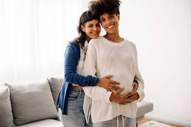 Young, diverse pregnant women in the third trimester stand together in a  studio. They wear jeans and bras, showcasing their baby bumps. Hugging and  looking at the camera, they represent a supportive