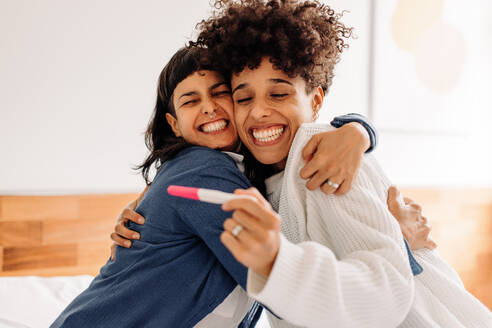 Celebrating having a baby on the way. Excited young lesbian couple smiling cheerfully and embracing each other after taking a home pregnancy test. Young female couple expecting a baby. - JLPSF04270