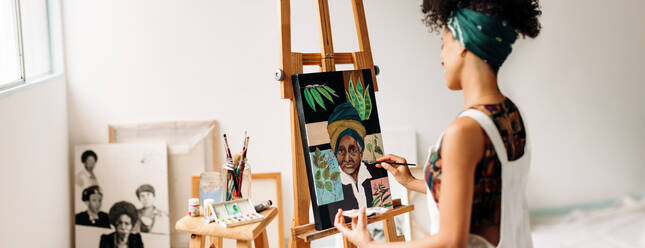 Young female painter working on a portrait painting in her studio. Happy young painter smiling while drawing her new artwork. Young woman working alone in her art studio. - JLPSF04286