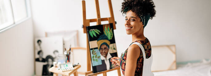 Confident female painter working in her studio. Happy young painter looking away with a smile on her face while drawing her new artwork. Young woman working alone in her art studio. - JLPSF04287