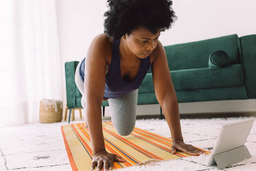 Reife Frau macht Übungen, während sie ein Online-Video ansieht. Afrikanische Frau macht Übungen zu Hause mit einem Tablet-PC. - JLPSF04331