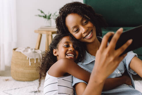 Frau mit Tochter macht ein Selfie mit Smartphone. Schöne Familie nimmt Selbstporträt im Wohnzimmer. - JLPSF04347