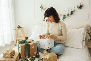 Woman sitting on bed with christmas presents. Woman celebrating christmas opening gift boxes. - JLPSF04438