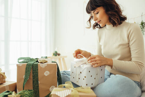 Nahaufnahme einer Frau, die auf dem Bett sitzt und Weihnachtsgeschenke verpackt. Frau sitzt auf dem Bett und trifft Vorbereitungen für Weihnachten. - JLPSF04439