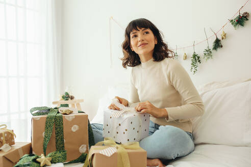 Frau auf dem Bett sitzend mit Weihnachtsgeschenken. Frau feiert Weihnachten zu Hause. - JLPSF04441