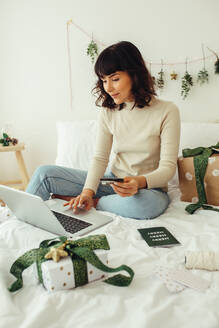 Woman sitting on bed using laptop computer for making credit card payment. Woman doing online shopping for christmas sitting at home. - JLPSF04474