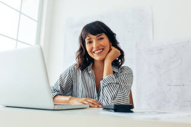 Close up of a smiling female entrepreneur. Businesswoman sitting at her desk working on laptop. - JLPSF04494