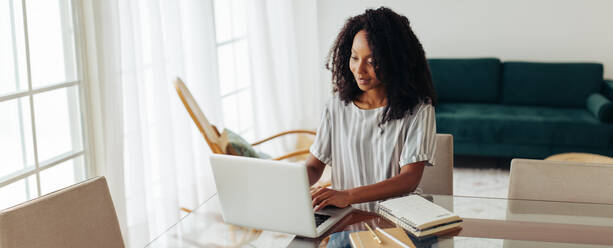 Junge Frau arbeitet zu Hause am Laptop. Afrikanische Frau sitzt am Tisch und arbeitet zu Hause am Laptop. - JLPSF04513