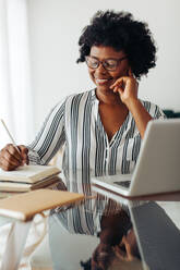 Frau sitzt zu Hause und schreibt Notizen. Weibliche Führungskraft macht sich Notizen bei der Arbeit im Home Office. - JLPSF04519