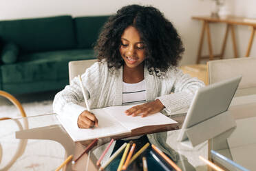 Young girl writing in her notebook at home. Girl sitting at table and completing her homework. - JLPSF04538