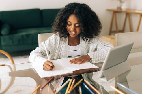 Junges Mädchen schreibt zu Hause in ihr Notizbuch, sitzt am Tisch und macht ihre Hausaufgaben. - JLPSF04538