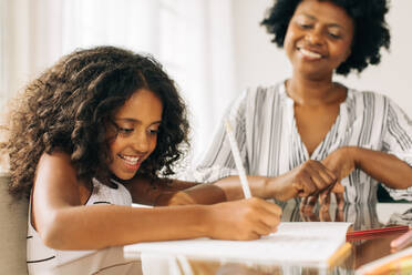 Mädchen schreibt ihre Hausaufgaben, während die Großmutter zusieht. Kleines Mädchen macht Hausaufgaben, während die Großmutter daneben sitzt - JLPSF04540