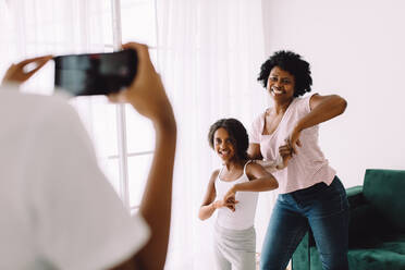Großmutter und Mädchen tanzen, während die Frau ihr Video mit dem Handy aufnimmt. Großmutter und Enkelin nehmen ihr Tanzvideo für soziale Medien auf. - JLPSF04566