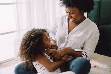 Grandmother playing with granddaughter at home. Girl and mature woman sitting together and playing on living room floor. - JLPSF04575