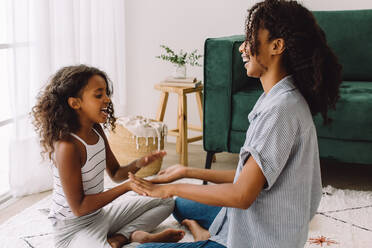 Mother and daughter playing patty cake together at home. Girl playing with mom while sitting on floor of living room. - JLPSF04592