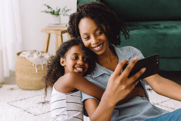 Mother and daughter taking selfie. Woman using cell phone to take self portrait with her cute girl at home. - JLPSF04593